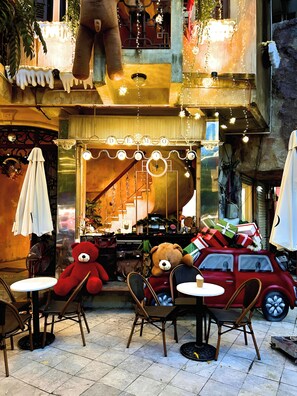 A cozy outdoor seating area with tables and chairs, a teddy bear, a toy car, and a large window with curtains. - DEMO Inn & Ine - Poetic Studio Stay (Hanoi)