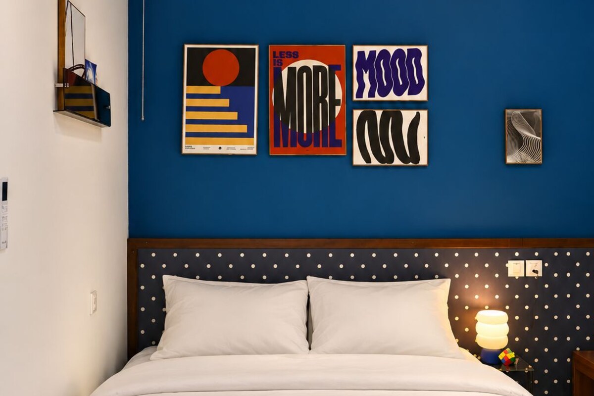 Un dormitorio con una pared azul, una cama con ropa de cama blanca y tres obras de arte enmarcadas.