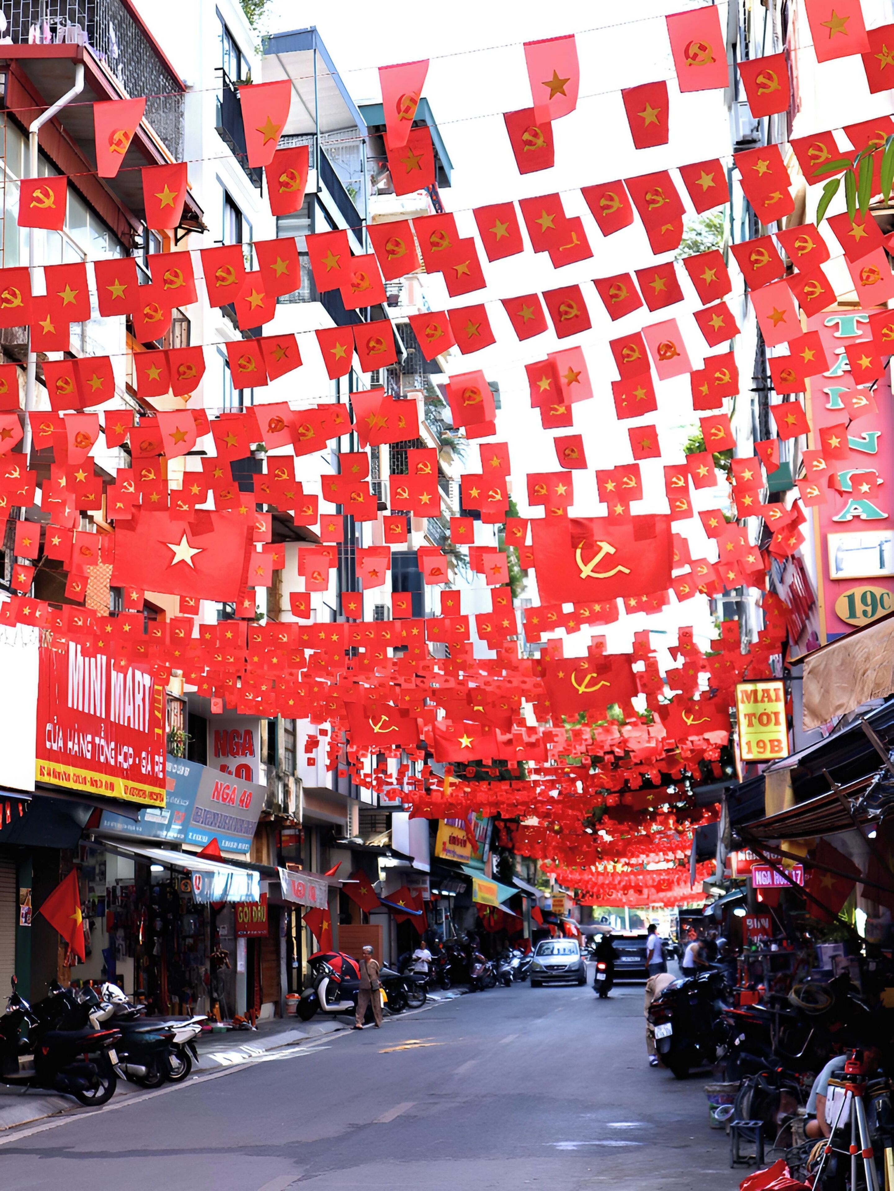 A street lined with shops and motorcycles, decorated with red flags.