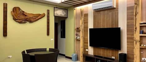Un salon doté d’un téléviseur à écran plat, d’un mur recouvert de panneaux en bois et d’un coin repas avec des chaises.