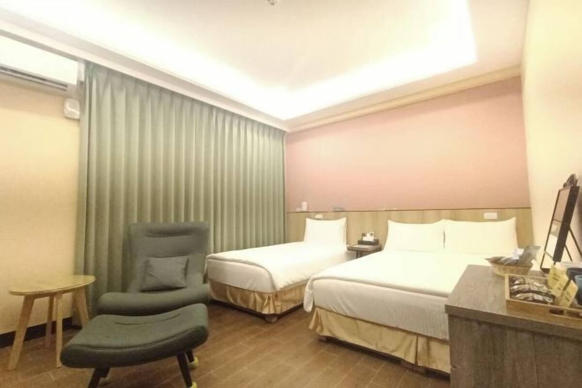 A hotel room with two single beds, a chair, a small table, and a desk with a mirror.