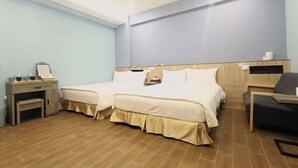 Habitación de hotel con una cama doble, un escritorio con silla, una mesita y un estante con artículos de aseo.