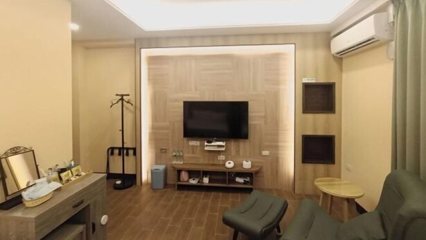 Una sala de estar moderna con un televisor de pantalla plana montado en una pared de madera, un sofá, una mesita redonda y un espejo sobre una consola de madera.