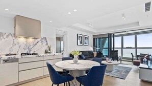 A modern kitchen with a marble backsplash, a dining area with a marble table, and a large window overlooking the sea. - Luxury Beachfront 1-Bed Apartment with Pool & Gym (Surfers Paradise)