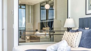 A modern bedroom with a large bed, a glass partition, and a view of a balcony. - Luxury Beachfront 1-Bed Apartment with Pool & Gym (Surfers Paradise)