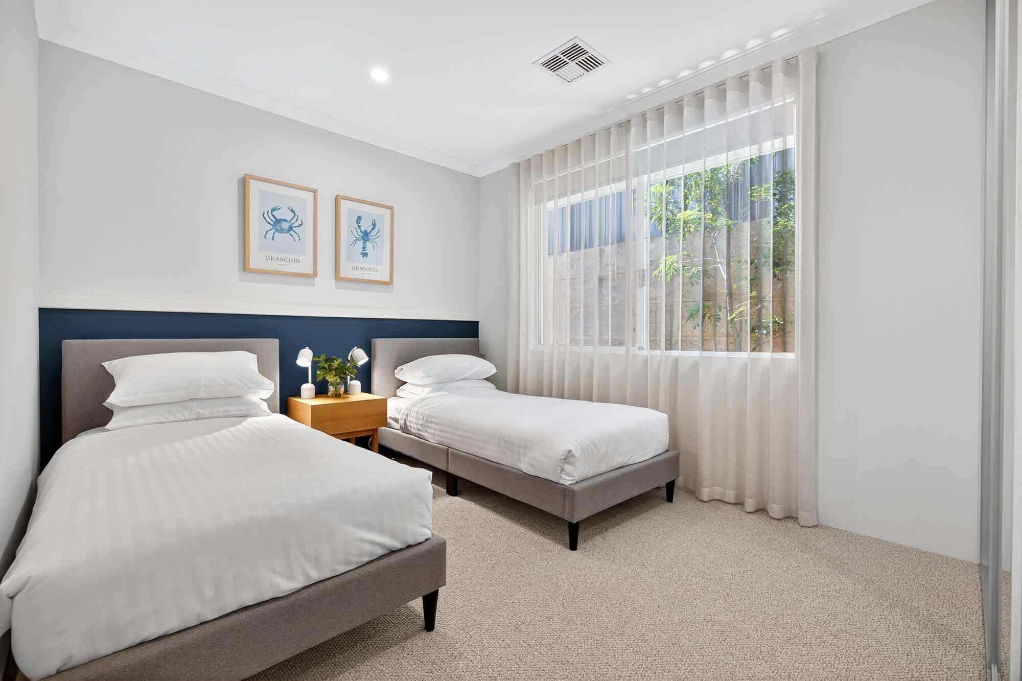 Habitación de hotel con dos camas, una mesita de noche y una ventana con cortinas traslúcidas.