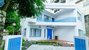 Een gebouw met twee verdiepingen, een blauw-wit kleurenschema, een balkon op de bovenverdieping en een geplaveid entreegebied.
