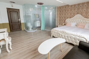 Une chambre avec un grand lit, une chaise blanche, un plancher en bois et une douche séparée par des parois en verre.