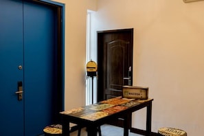 Un couloir avec une porte bleue, une table sur laquelle est posé un jeu de société et une porte avec une pancarte.