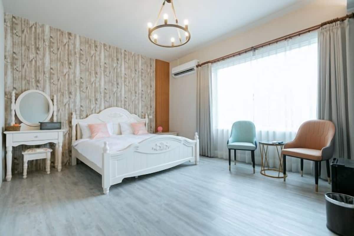 Un dormitorio con cama, tocador con espejo, silla y ventana con cortinas.