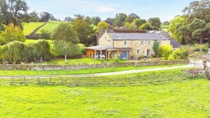Een stenen huis met een veranda, omgeven door weelderige groene velden en bomen.