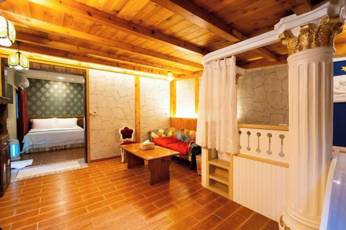 Une pièce avec un plafond en bois, un lit, un canapé, une table et un miroir orné d’une colonne décorative.