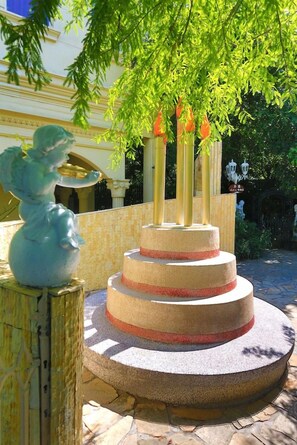 A multi-tiered stone fountain with a statue of an angel on a pedestal, surrounded by greenery and a building in the background. - Xinyuan My Dream Castle (Yilan)