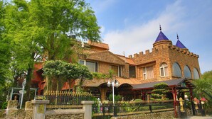 Un edificio de estilo castillo con fachada de piedra, ventanas de arco y una torre destacada con techo puntiagudo.