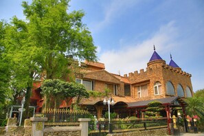 Un edificio de estilo castillo con fachada de piedra, ventanas de arco y una torre destacada con techo puntiagudo.
