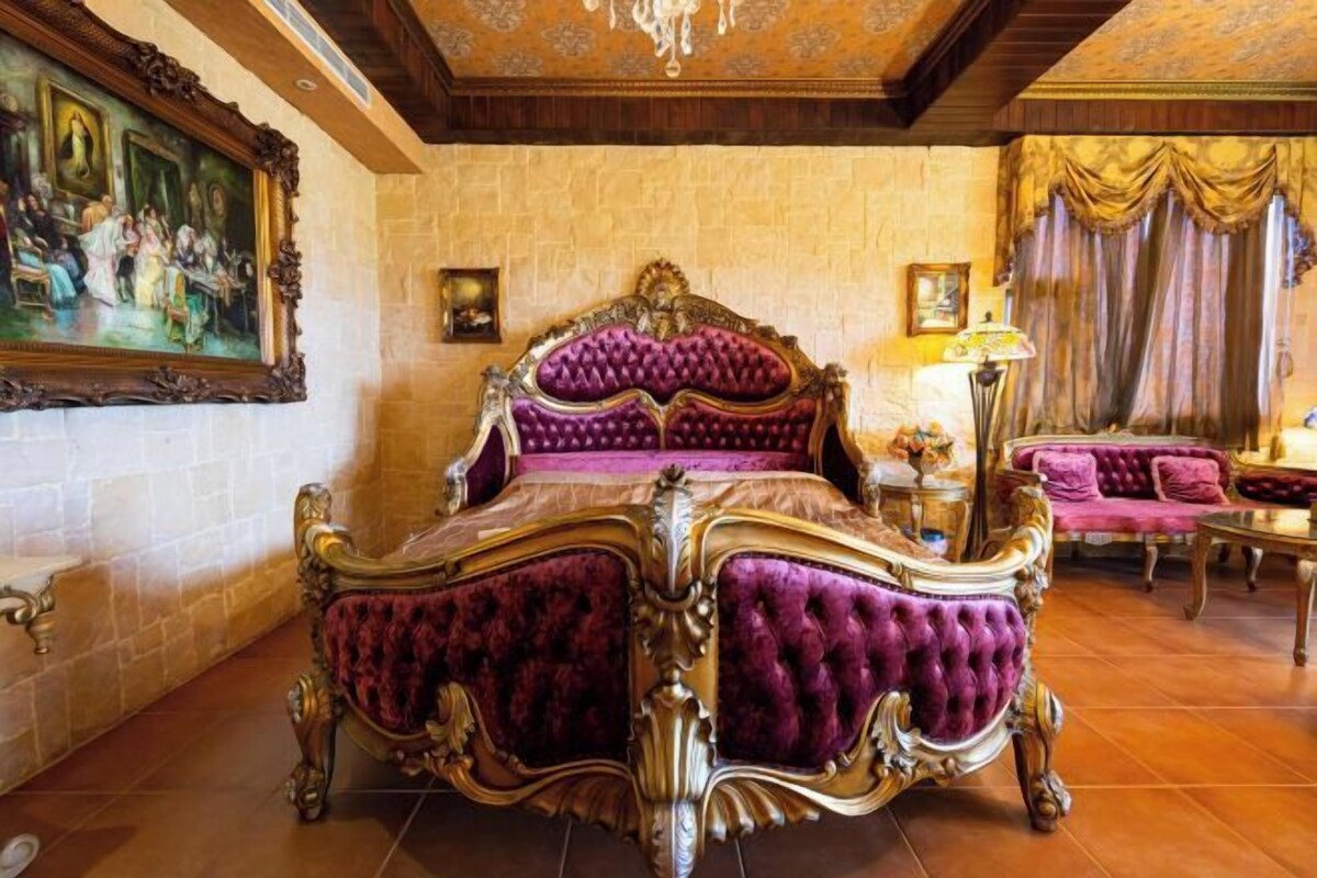 Une chambre à coucher luxueuse, avec un grand lit somptueux, un tableau au mur et un lustre classique.