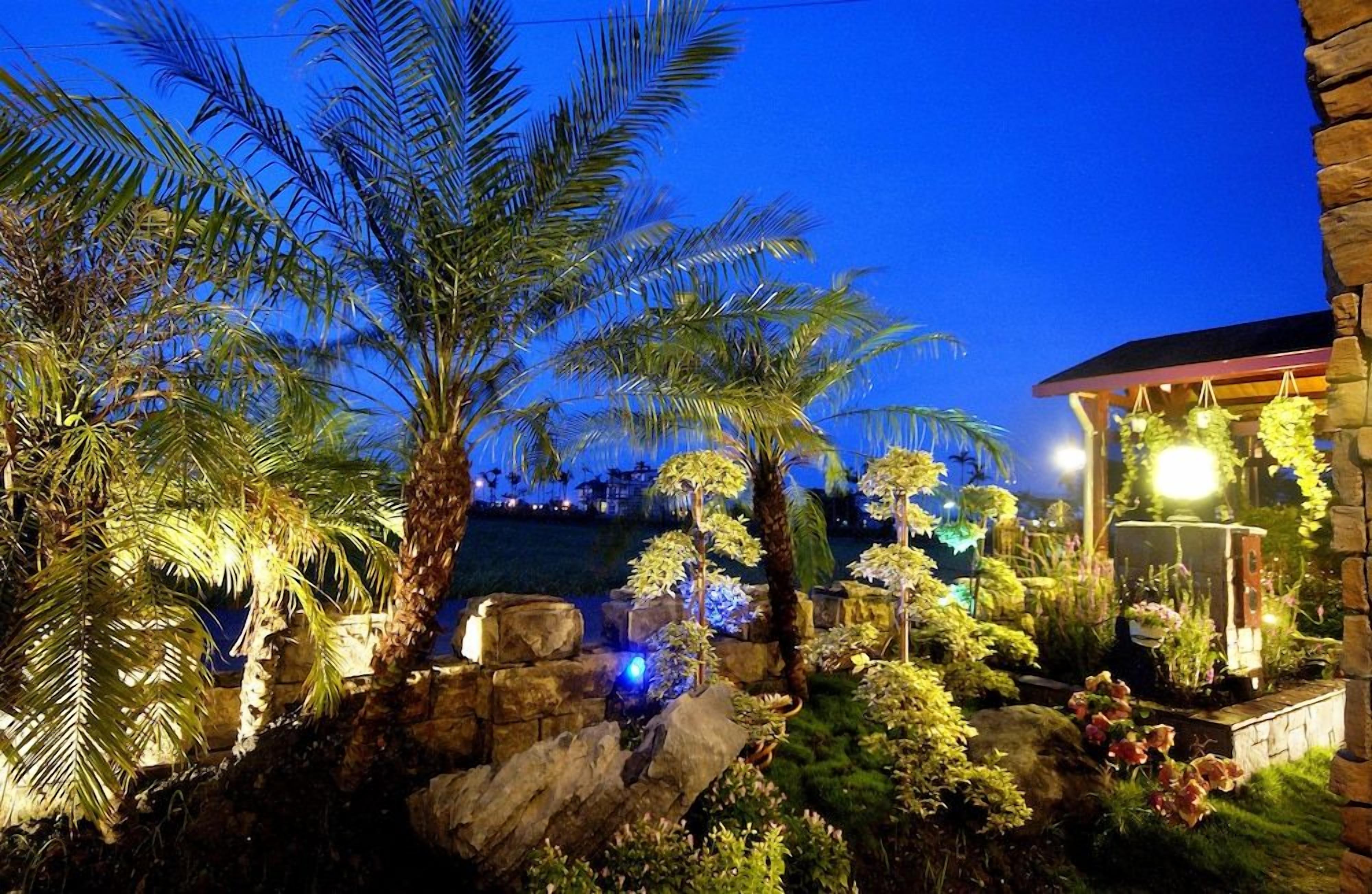 A well-lit garden with palm trees and a stone building.