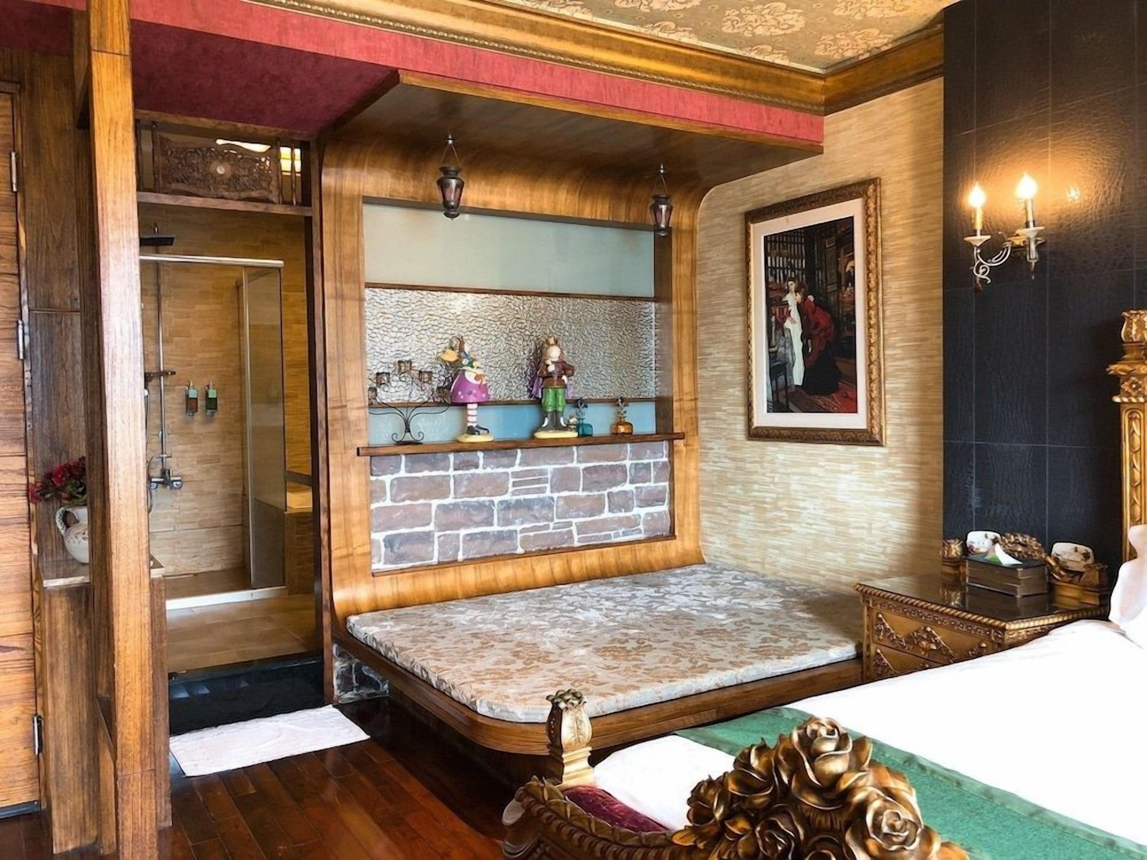 Um quarto com uma cama, um banco de madeira, prateleira com pequenos objetos decorativos, um quadro emoldurado e uma porta que dá para o banheiro.