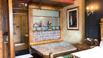 Um quarto com uma cama, um banco de madeira, prateleira com pequenos objetos decorativos, um quadro emoldurado e uma porta que dá para o banheiro.