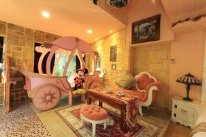 A room with a stone wall, a pink carriage, a Mickey Mouse figure, a table with a floral tablecloth, and a patterned rug. - Xinyuan My Dream Castle (Yilan)