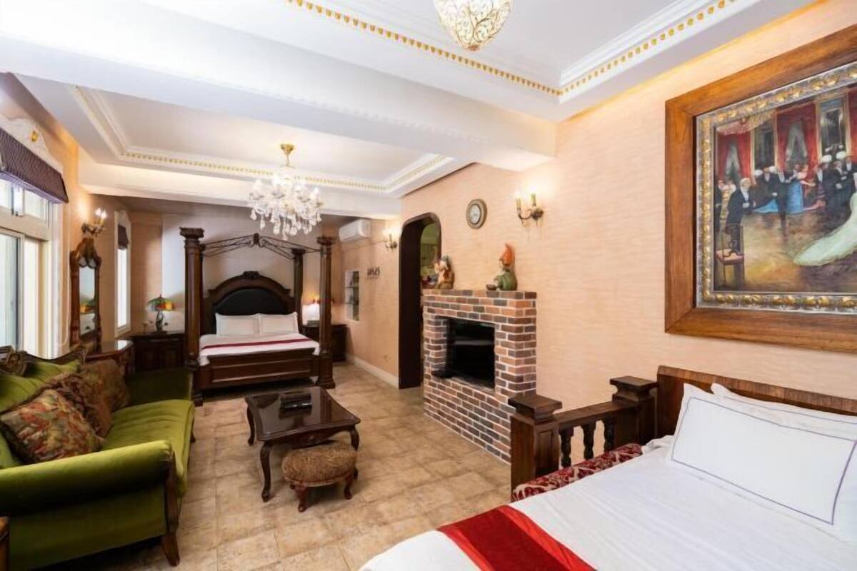 Een slaapkamer met een hemelbed, een openhaard, een groene bank en een groot schilderij aan de muur.