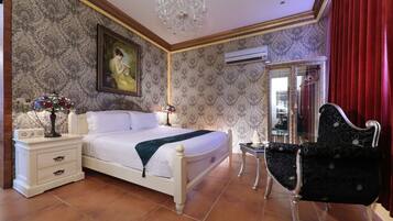 A bedroom with a bed, bedside tables, a chandelier, a mirror, and a chair.