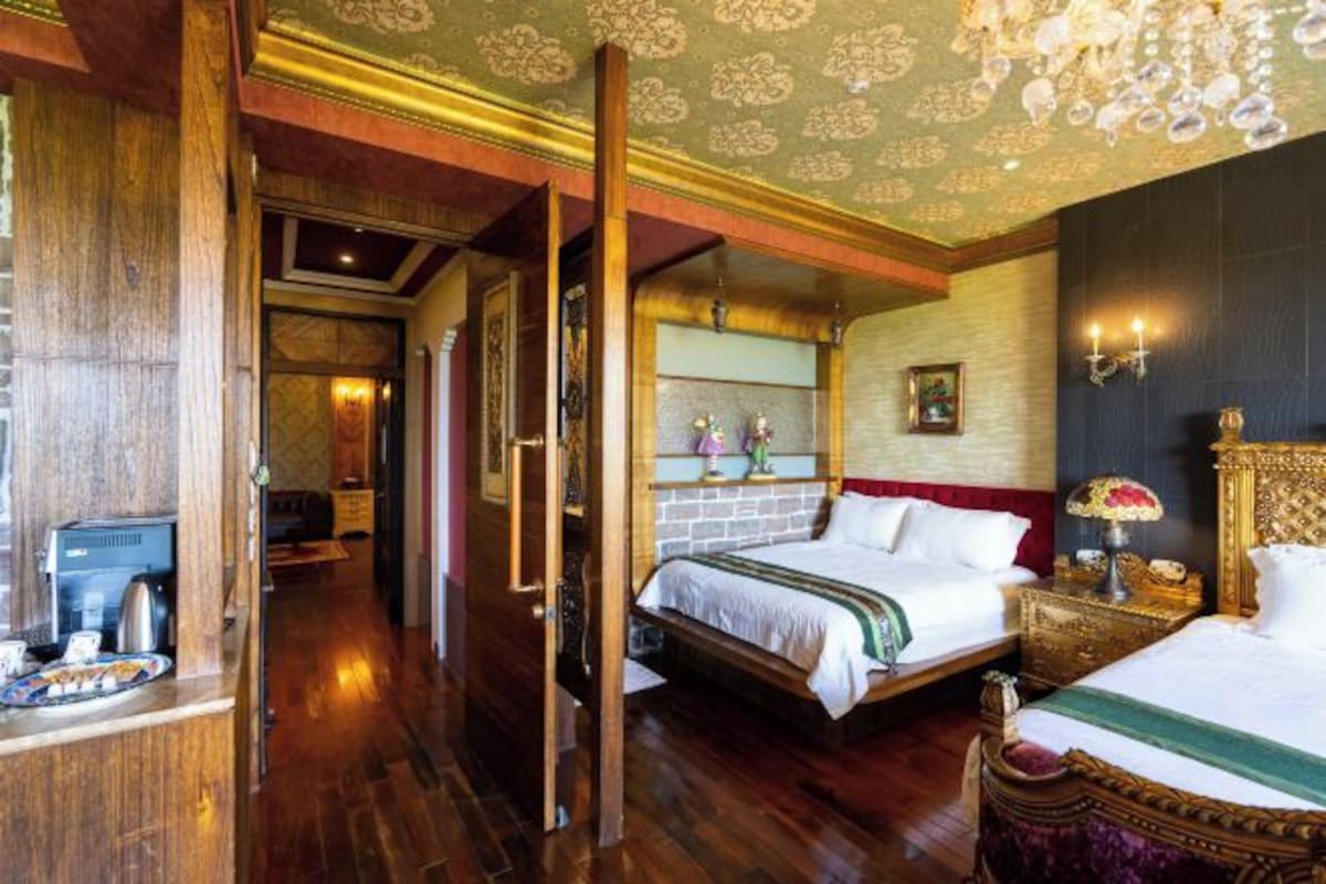 A hotel room with a large bed, a wooden floor, a chandelier, and a television.