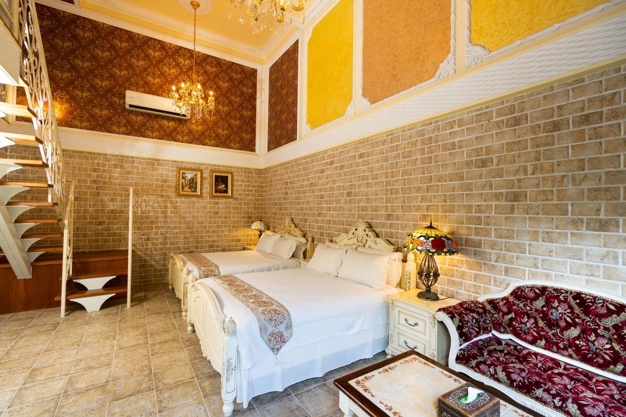 Une chambre d’hôtel avec un mur en briques, deux lits, un lustre et un escalier.