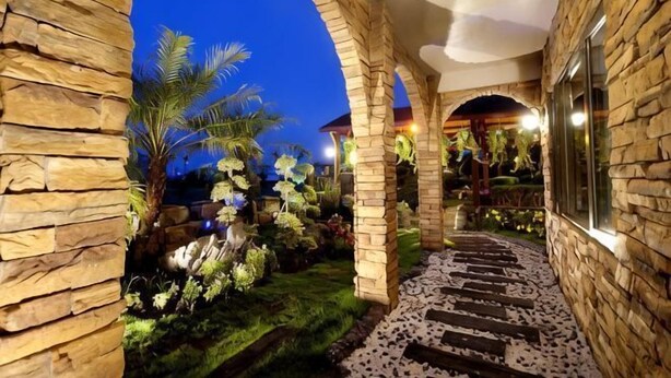 A stone archway leading to a garden with a stone pathway and palm trees. - Xin Yuan-My Dream Castle (Yilan)