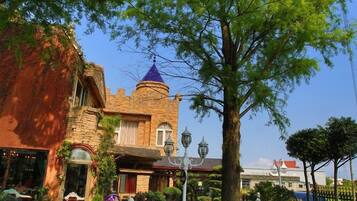 A castle-like building with a tower, surrounded by lush greenery and a paved pathway.
