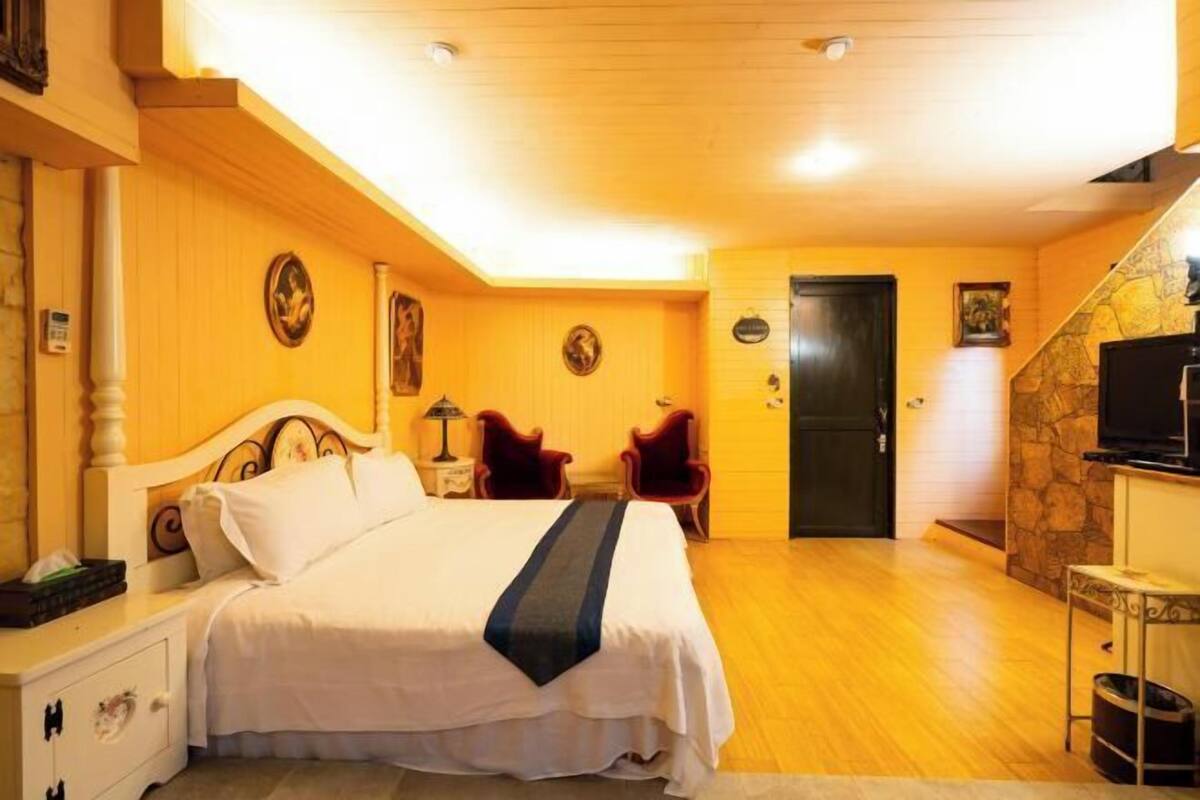 Een slaapkamer met een bed, nachtkastjes, een stoel, een televisie en een stenen muur.
