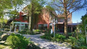 Ein Gartenweg führt zu einem Gebäude mit roter Fassade und einer weißen Laube.