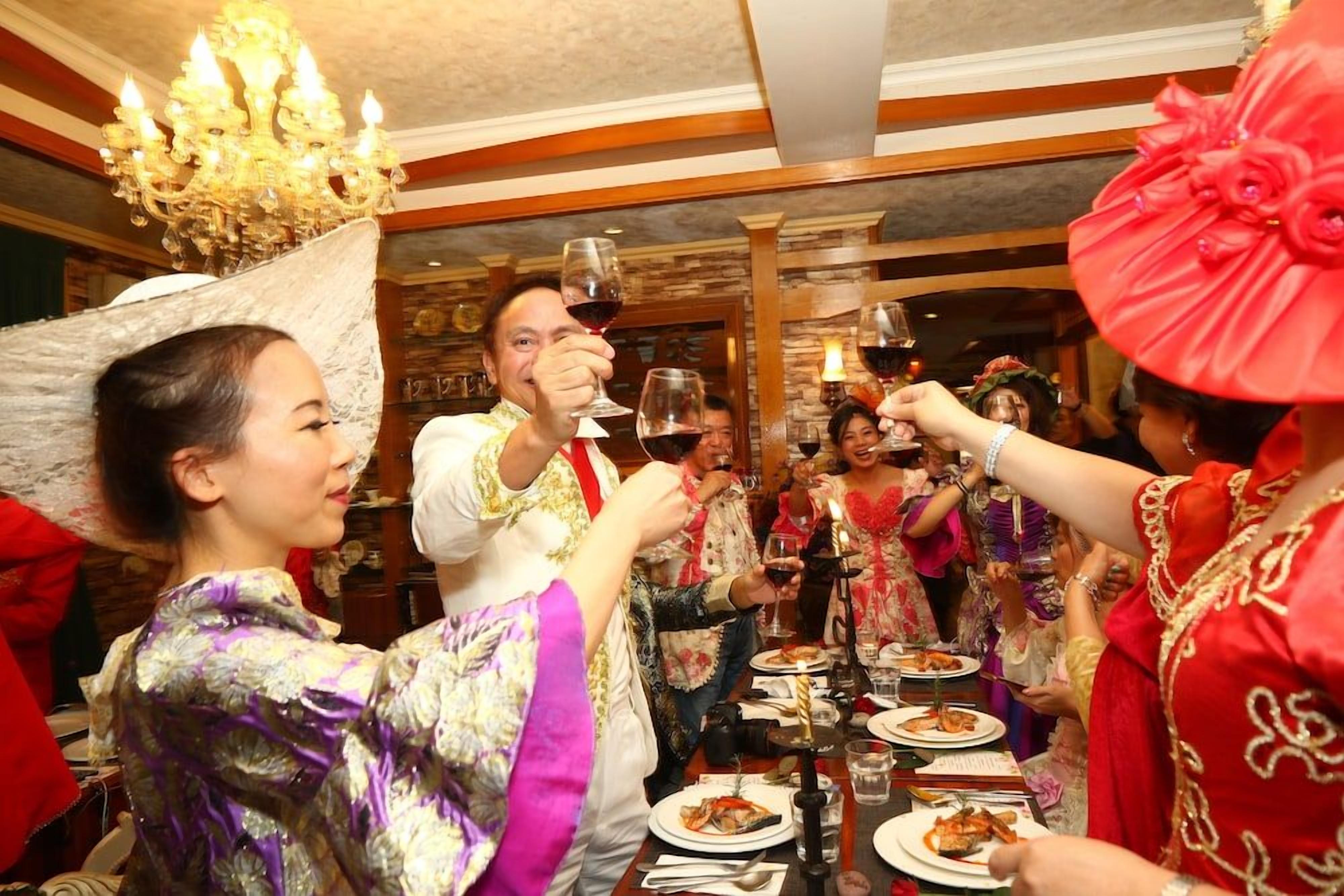 A group of people toasting with wine glasses at a dinner table in a room with wooden paneling and a chandelier.