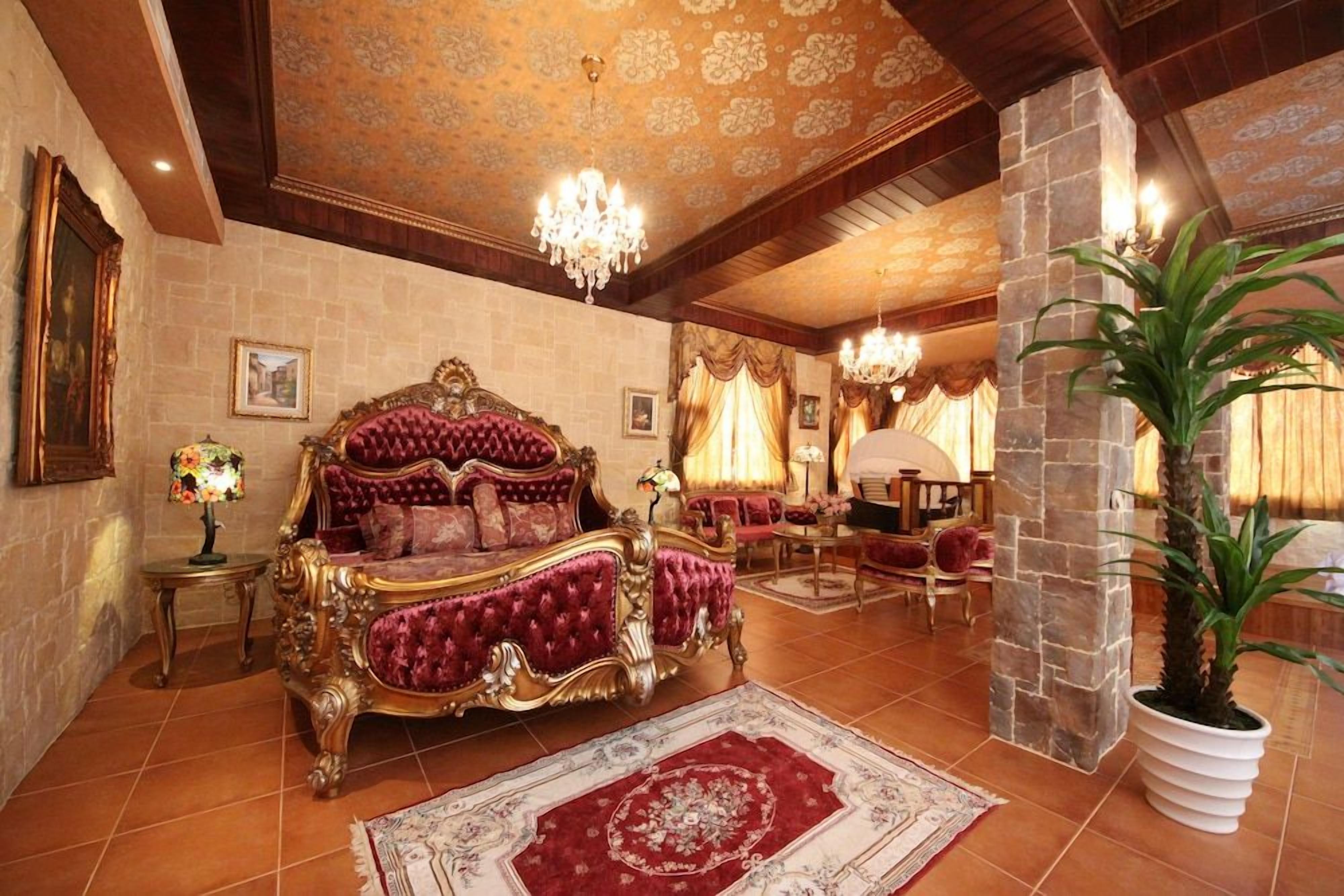 A luxurious bedroom with a large ornate bed, a chandelier, and a stone pillar.
