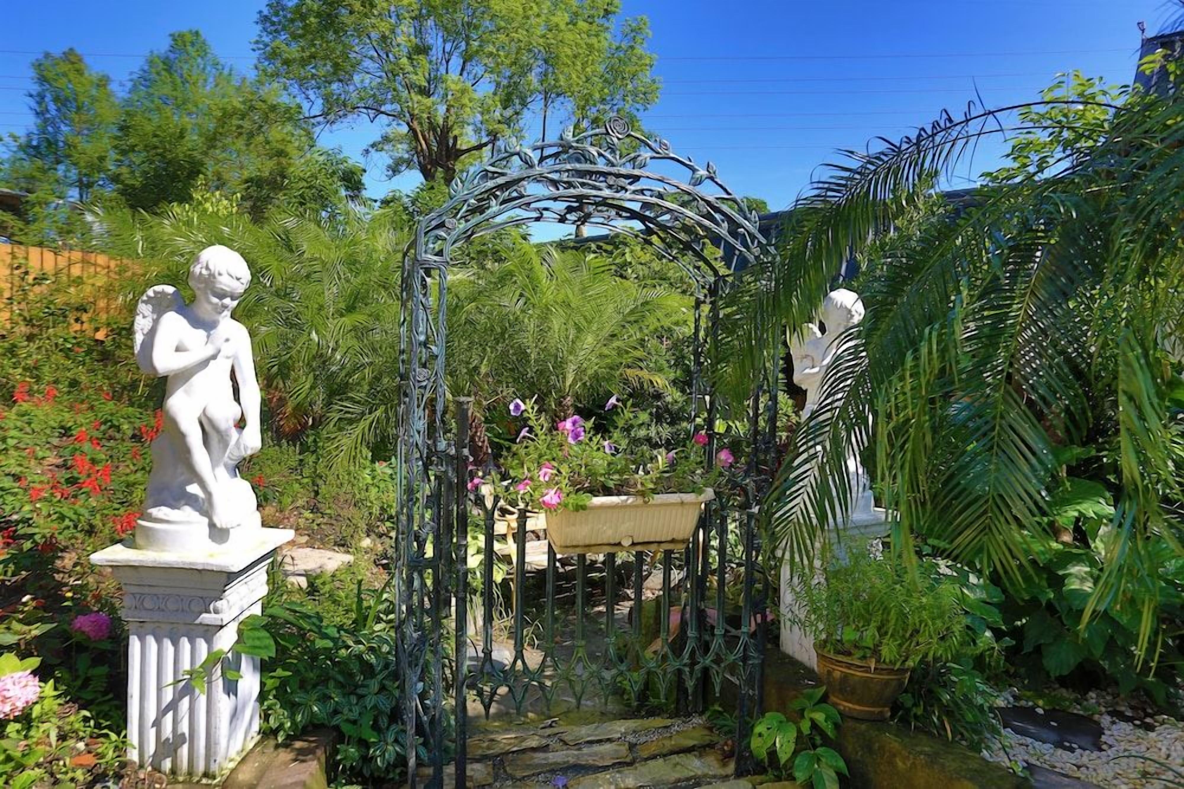 Un jardin agrémenté d’une arche en métal, de statues et d’une végétation luxuriante.