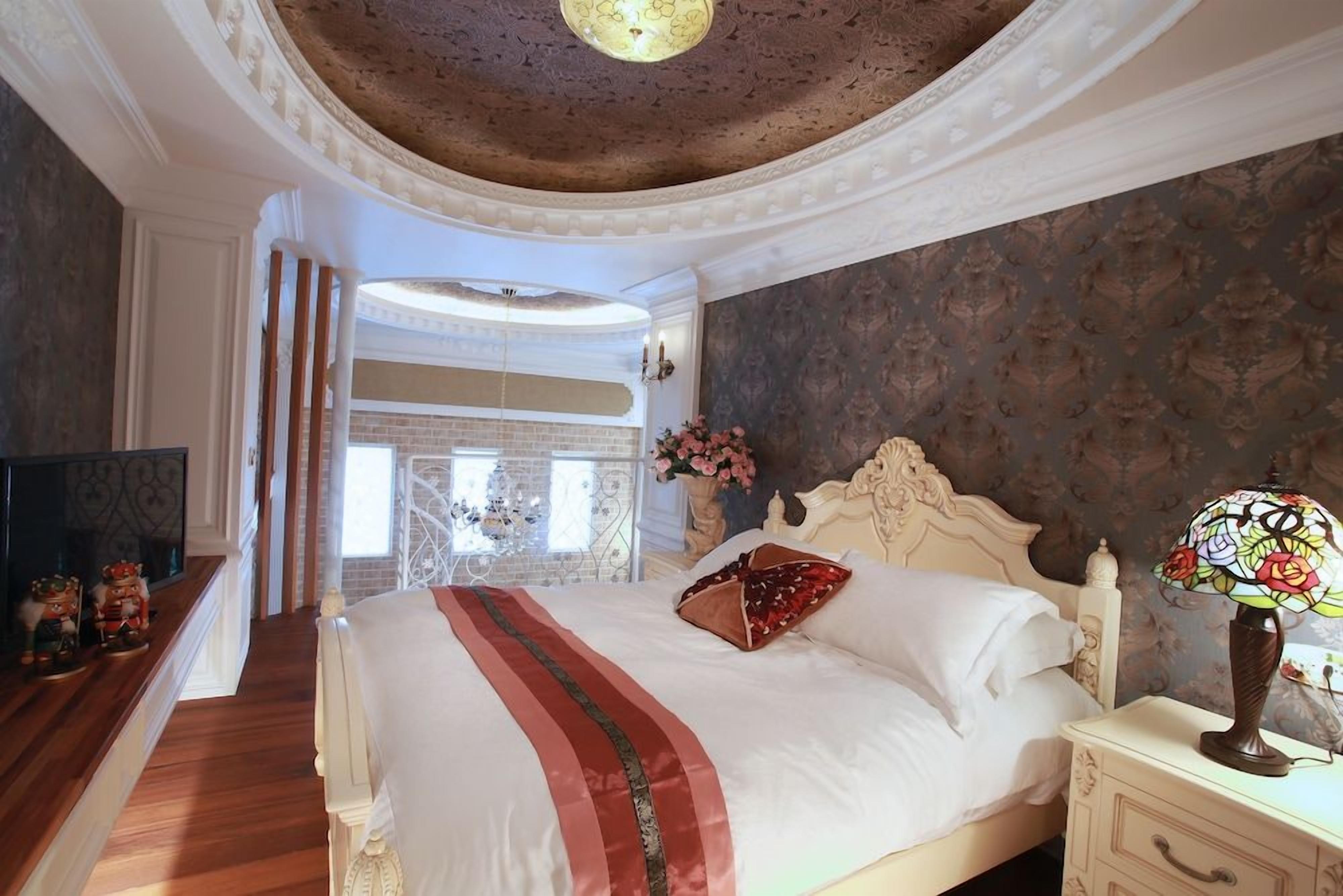 A bedroom with a large bed, a nightstand with a lamp, and a view of a brick wall.