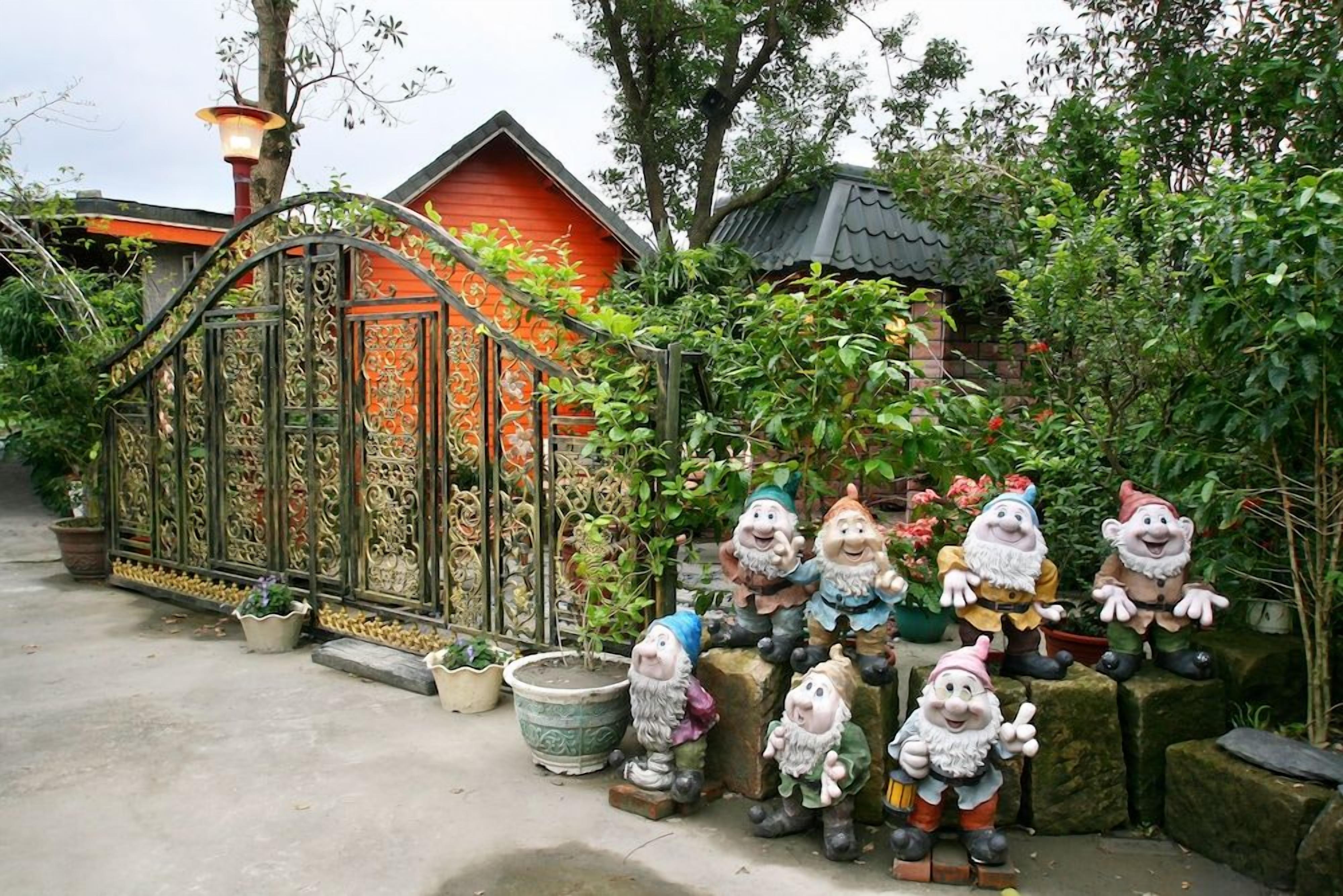 Un jardín con estatuillas de gnomos decorativos y una reja de hierro forjado.