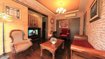 Sala de estar com parede de tijolos, televisão, poltrona vermelha, mesa de centro de madeira e um candelabro.