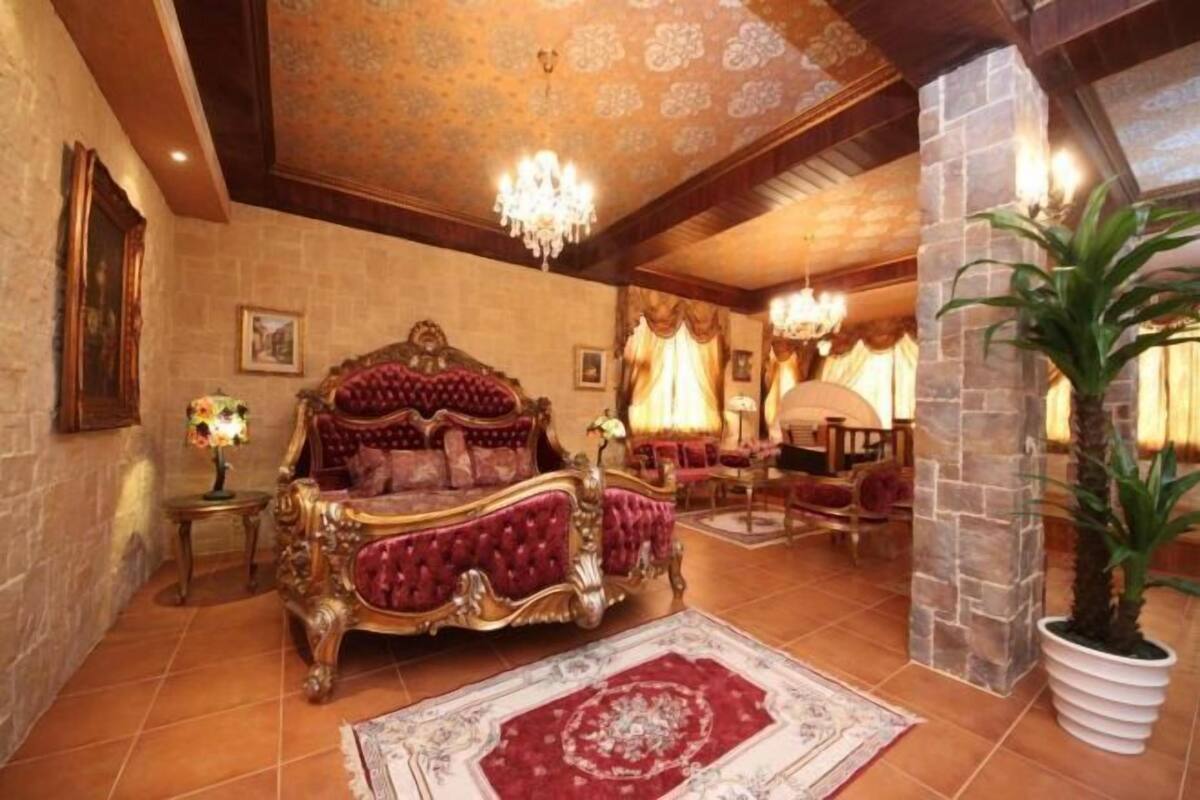 Een luxueuze slaapkamer met een groot, versierd bed, een kroonluchter en een stenen zuil.