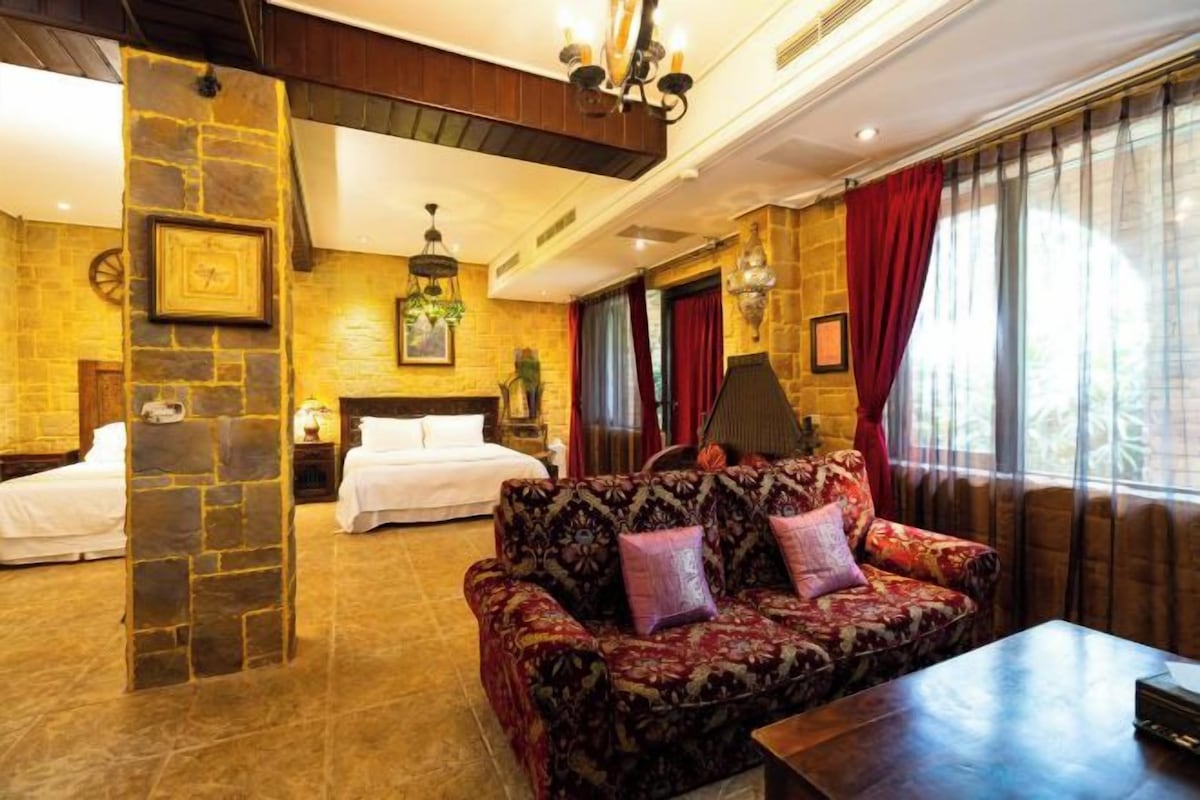 Une chambre d’hôtel avec un mur décoratif en pierre, un canapé à motifs floraux, un lit et une grande fenêtre avec des rideaux.