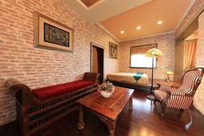 A room with a brick wall, a wooden bench with a red cushion, a wooden table with a vase of flowers, a striped armchair, and a bed with a green blanket. - Xinyuan My Dream Castle (Yilan)