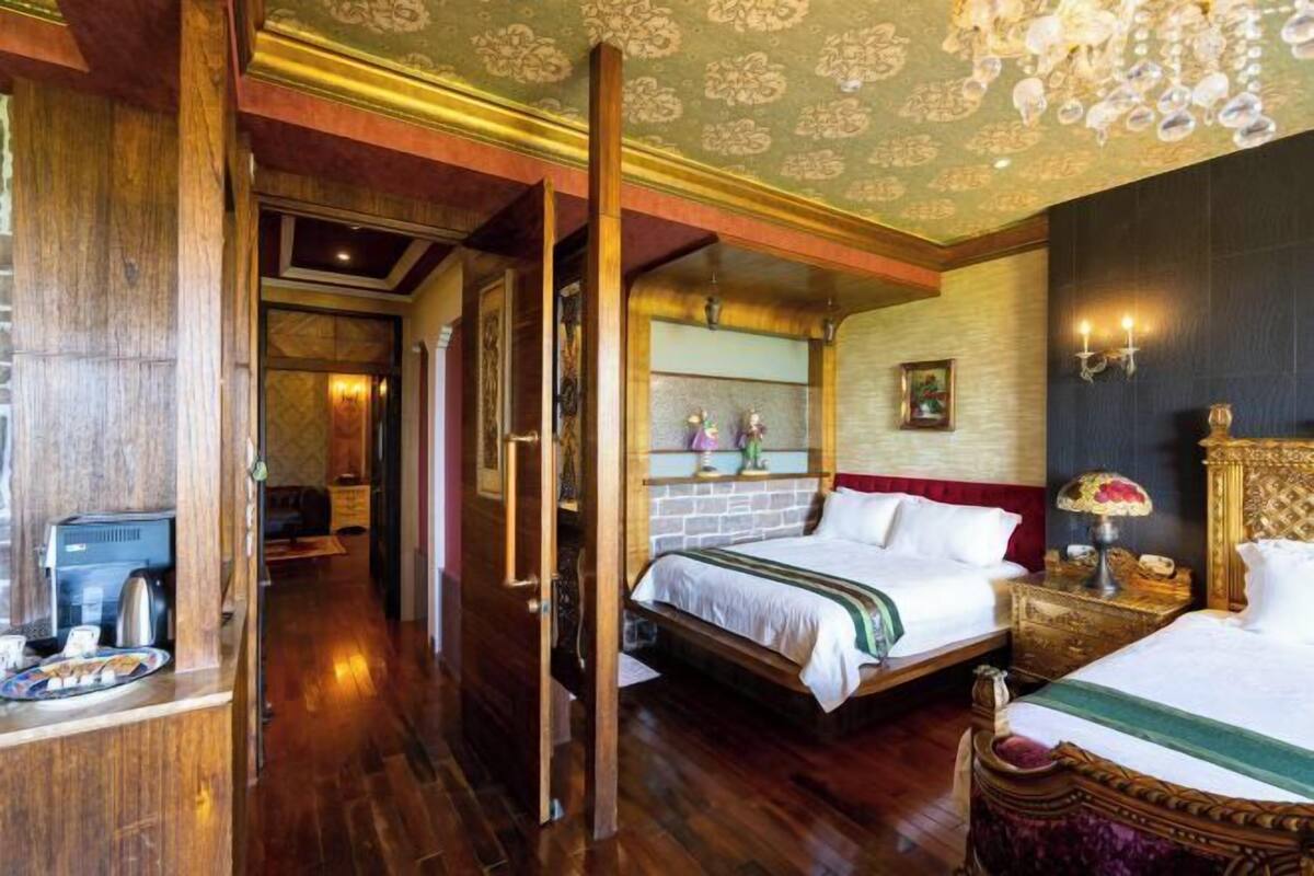 Een hotelkamer met een houten vloer, een bed met wit beddengoed, een nachtkastje met een lamp en een kroonluchter.