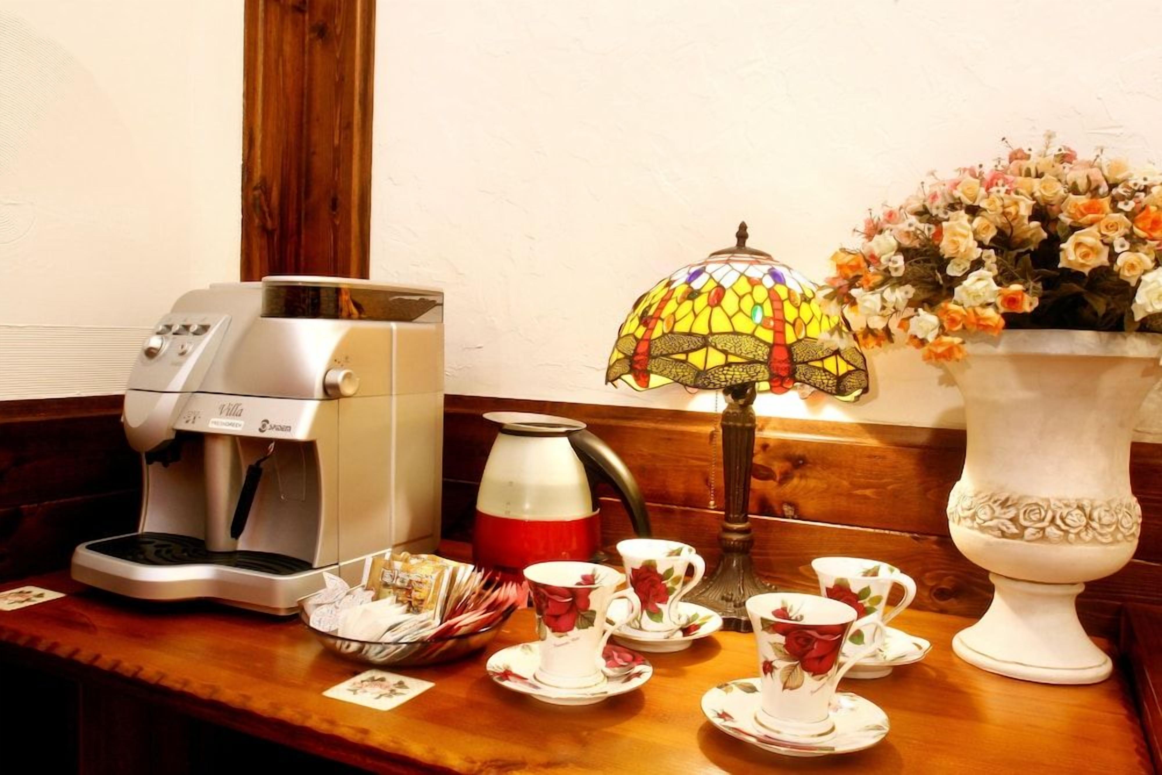 A coffee machine, teapot, teacups, teapot, and a vase with flowers on a wooden table.