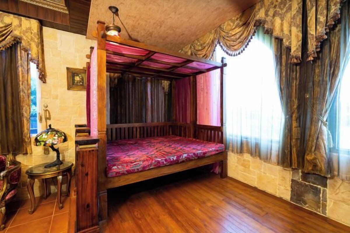 Ein Zimmer mit einem Himmelbett, einem Kamin aus Stein und einem kleinen Tisch mit einer Lampe.