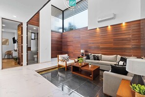 Ein modernes Wohnzimmer mit einer Couch, Sesseln und einem Couchtisch. Es gibt Holzpaneele an der Wand und ein Fenster mit Jalousien.
