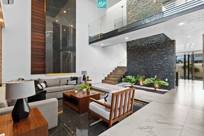 Eine moderne Lobby mit einer Couch, einem Couchtisch und einem Holzstuhl. Eine Treppe mit Steinwand und Glasgeländer ist ebenfalls vorhanden.