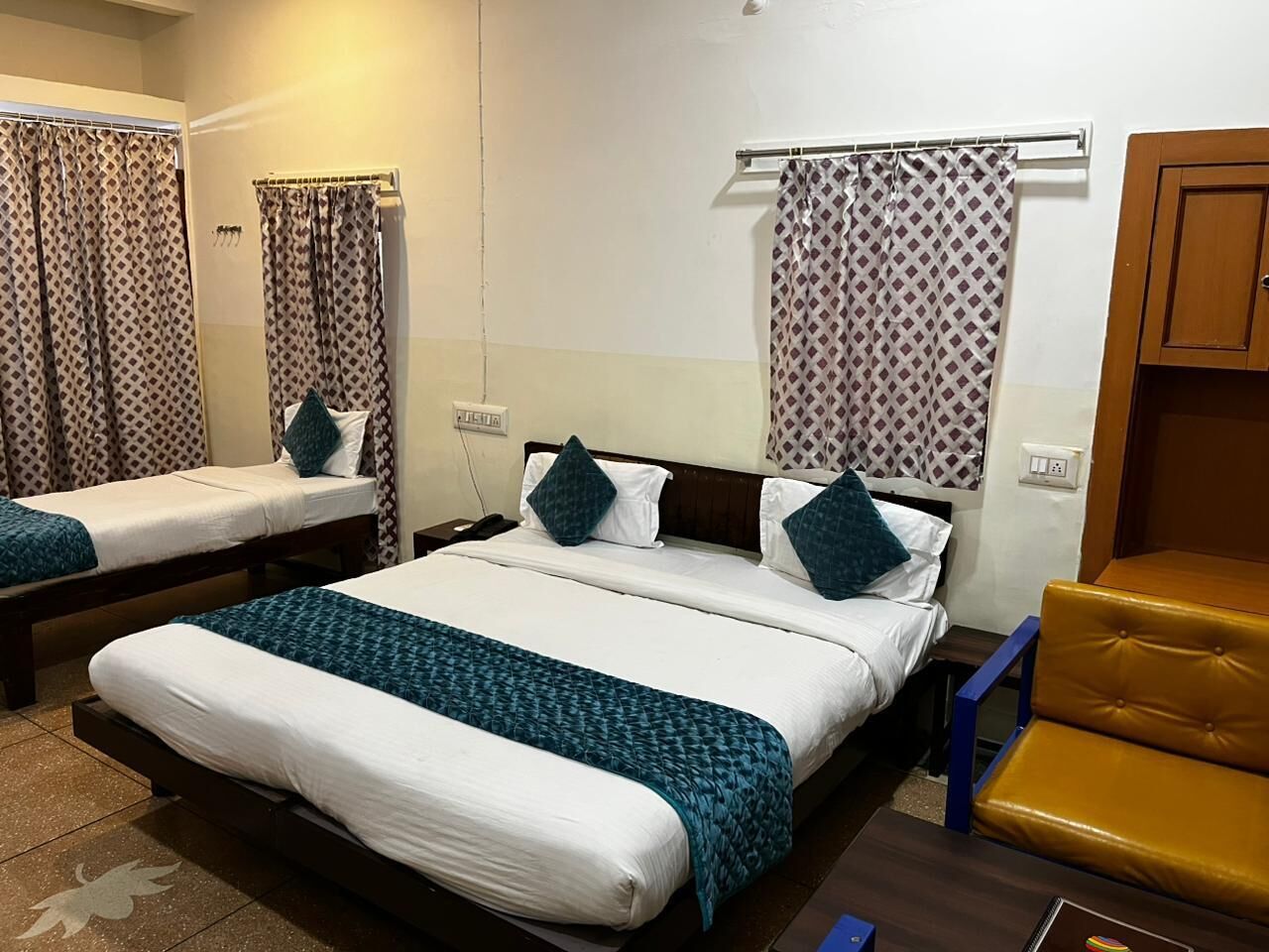 Una habitación de hotel con dos camas individuales, una cama grande, un armario de madera y una silla amarilla.