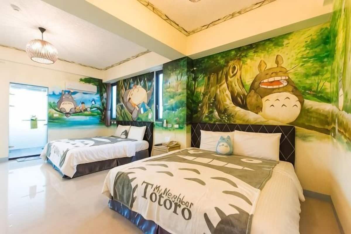A hotel room with two beds, a mural of Totoro, and a large window.