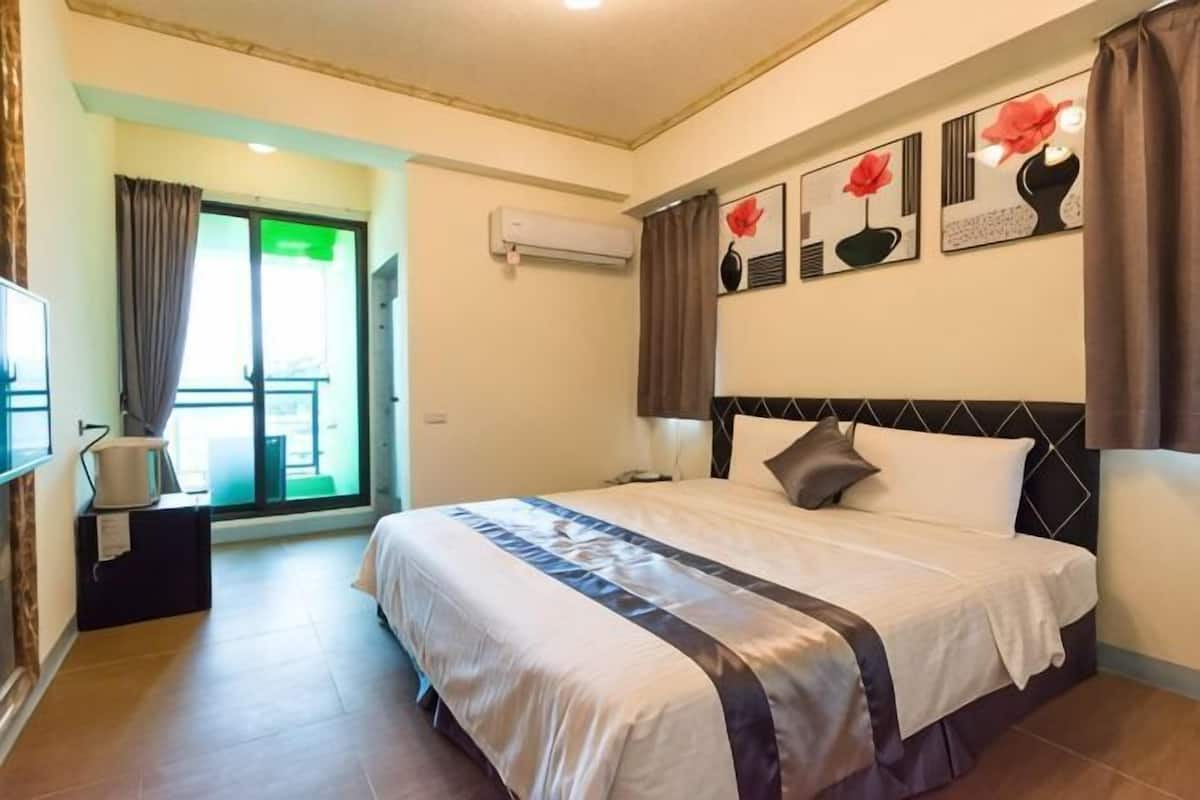 A hotel room with a bed, a TV, a window with curtains, and artwork on the wall.