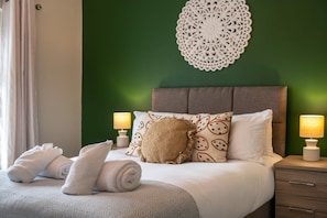 Un lit bien fait, avec des serviettes pliées, un plaid à motifs et deux coussins décoratifs.